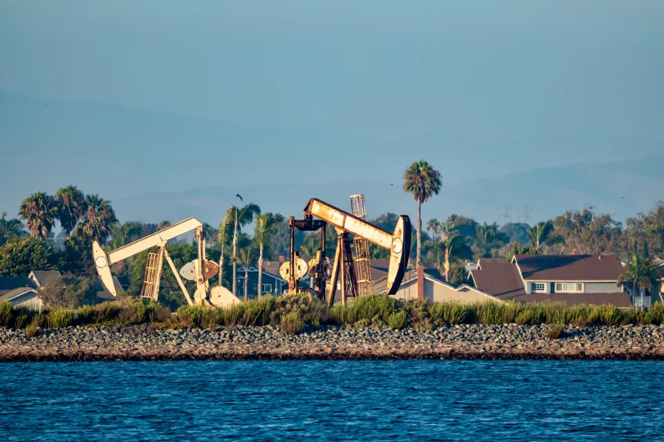Oil drilling pumps on a wetland beach in California with houses in background